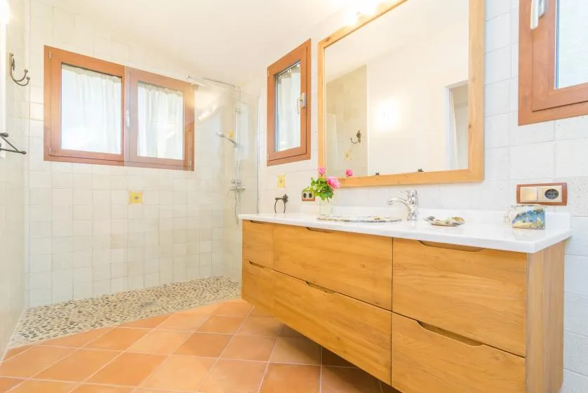 Un baño luminoso tiene un amplio tocador, un espejo grande y suelo de baldosas.