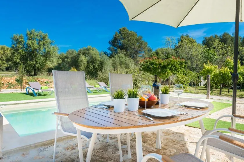Una mesa de comedor al aire libre junto a una piscina, con árboles al fondo.