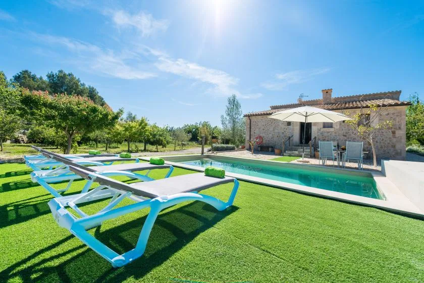 Una piscina al aire libre junto a una casa de piedra, con tumbonas sobre el césped.