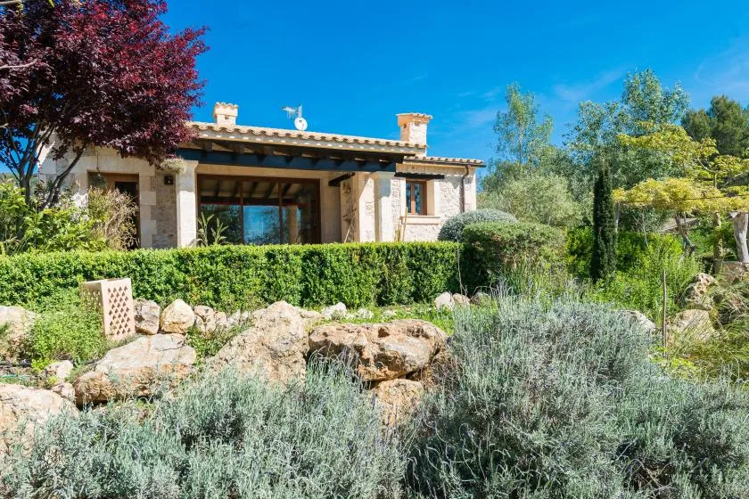 Una casa de piedra se alza detrás de un seto bajo y un jardín rocoso.