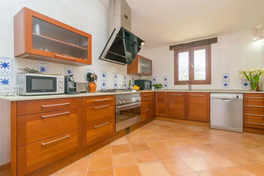 Una cocina amplia con gabinetes de madera, suelo de baldosas y una ventana sobre la encimera.