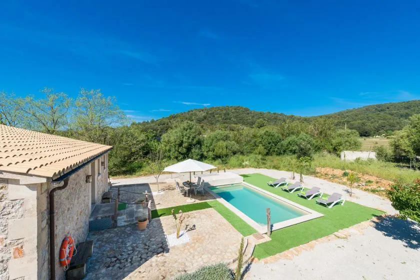 Piscina al aire libre junto a un edificio de piedra, con colinas verdes al fondo.
