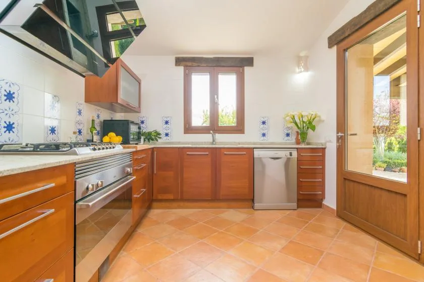 Una cocina luminosa con gabinetes de madera, suelo de baldosas y una ventana sobre el fregadero.