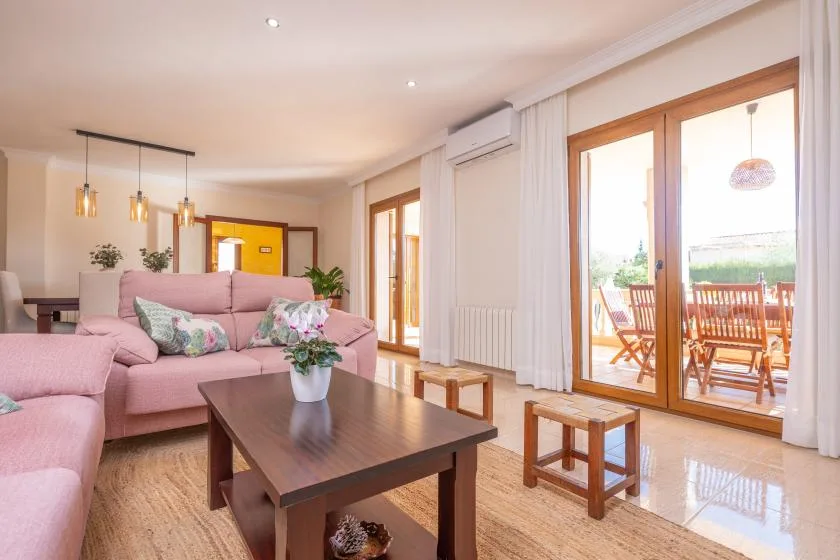 A bright living room has pink seating, a coffee table, and glass doors opening onto a furnished patio.