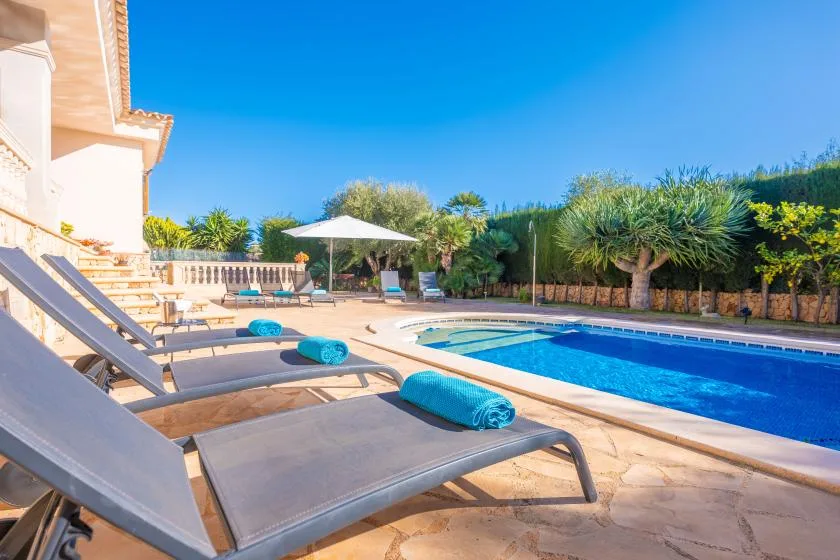 An outdoor pool beside a sunny patio with lounge seating and greenery.