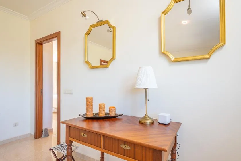 A wooden writing desk sits beneath gold-framed mirrors in a bright room.
