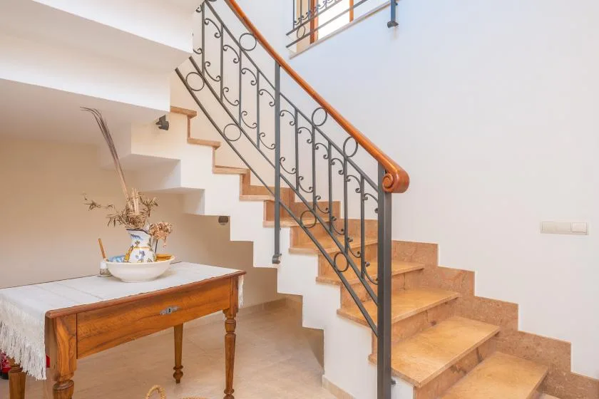 A staircase with a decorative metal railing rises beside a small wooden table.