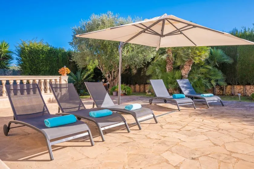 A sunny patio has reclining loungers beneath a large shade umbrella.