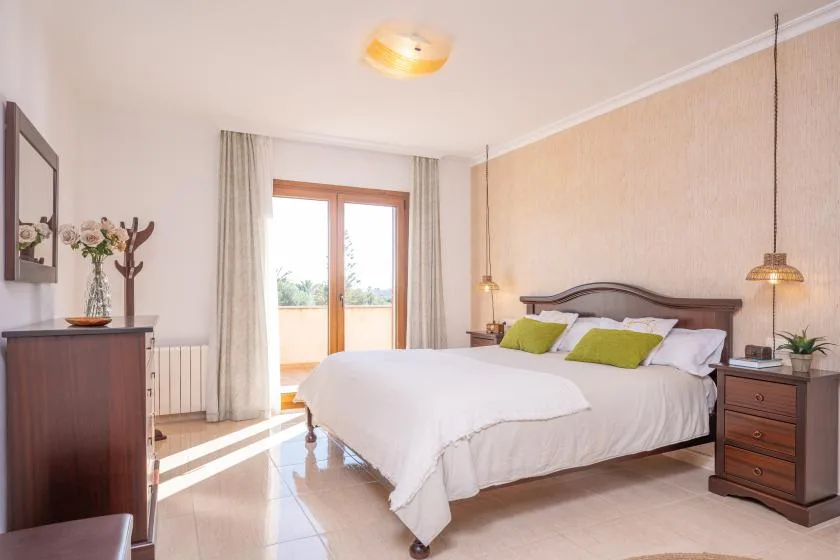 A bedroom with a neatly made bed and green accent pillows.
