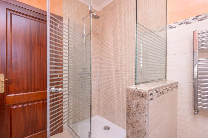 A tiled bathroom with a glass shower and a wooden door.