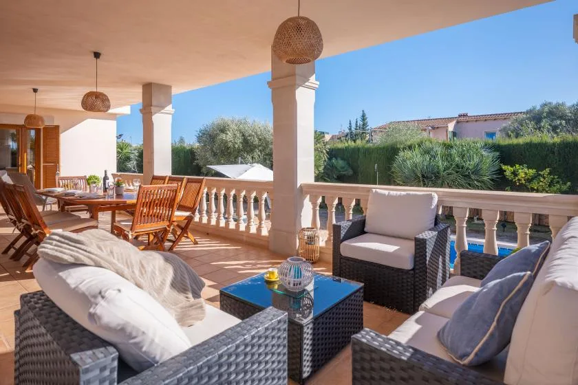 A covered outdoor terrace with wicker seating and a dining table overlooks a garden.