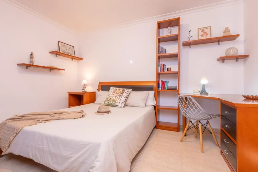 A bedroom with a bed and a built-in desk and shelving.