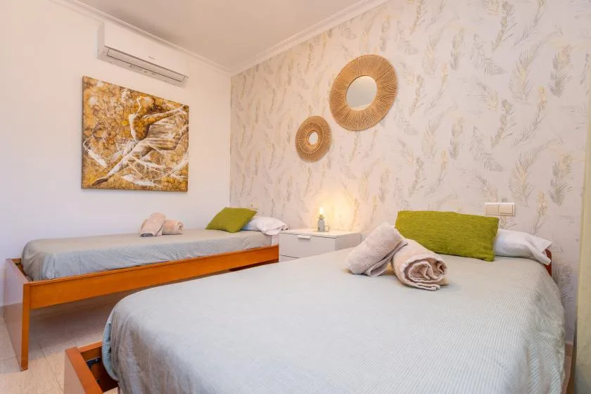 A bedroom with two beds, pale bedding, and leafy patterned wallpaper.