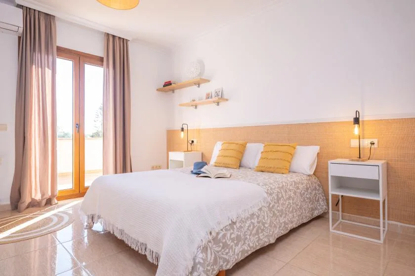 A bright bedroom with a neatly made bed and glass doors opening to a balcony.