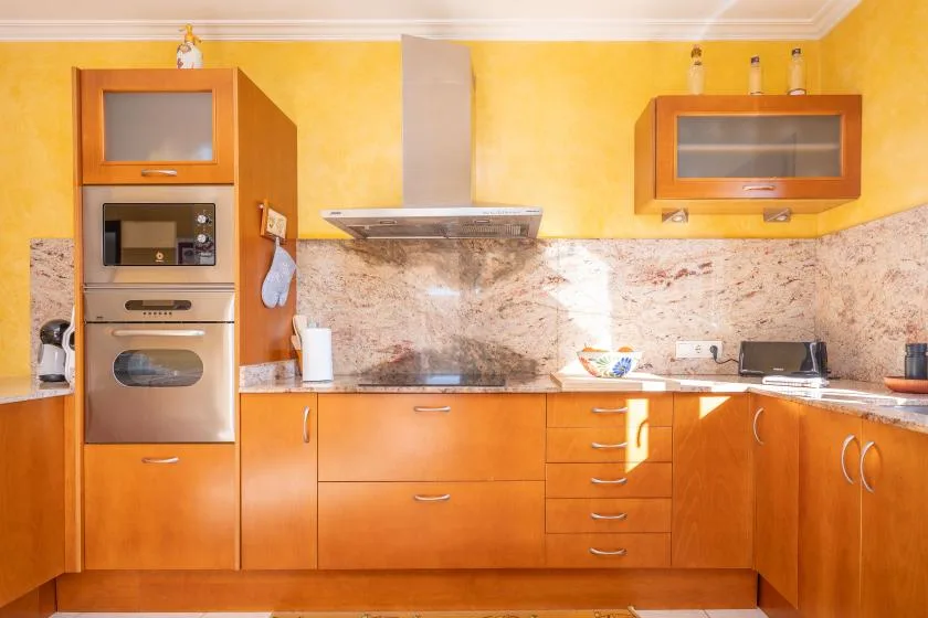A fitted kitchen with orange cabinetry, a built-in oven, and a range hood.