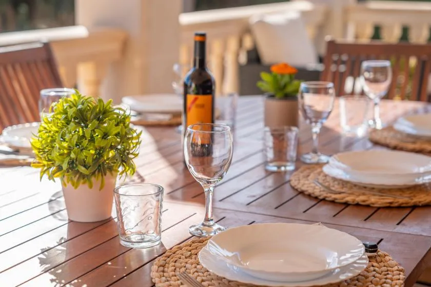 A dining table is set with plates, glasses, and small potted plants.