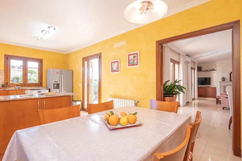 A bright dining area with a table, orange seating, and an open doorway to the kitchen.