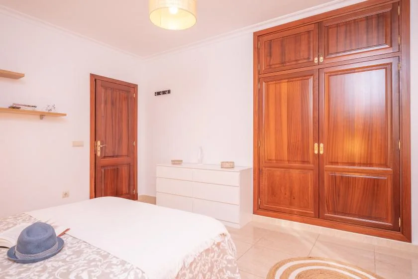 A bedroom with a bed, a wooden wardrobe, and a chest of drawers.
