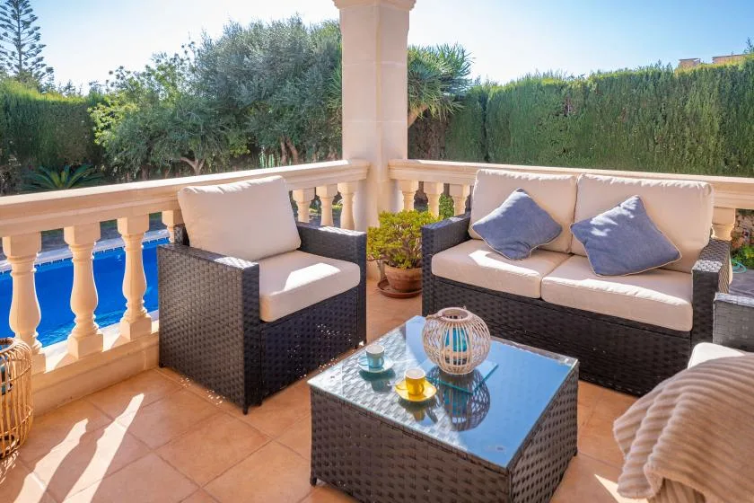 A furnished terrace with cushioned seating and a glass-topped table beside a pool.