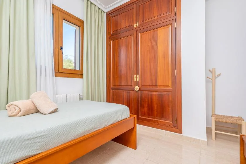A bedroom with a bed beside a wooden wardrobe and a window.