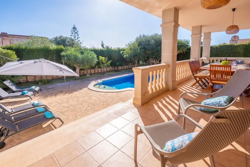 A sunny patio with outdoor seating overlooks a swimming pool and garden.
