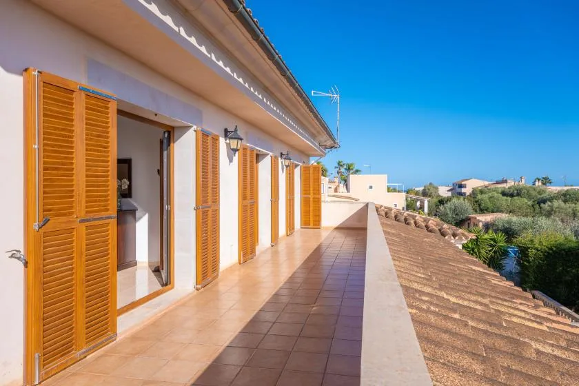 A tiled outdoor terrace runs alongside a building with open wooden shutters.