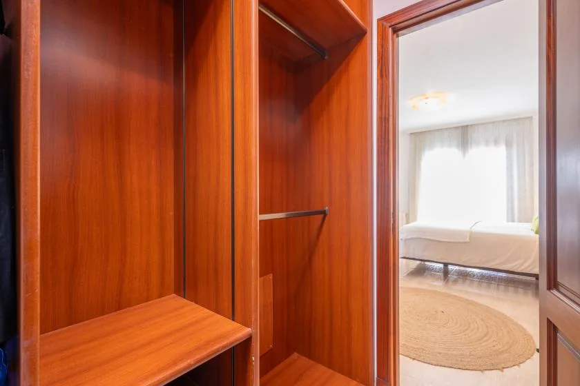 A wooden wardrobe opens onto a bedroom with a bed and round rug.