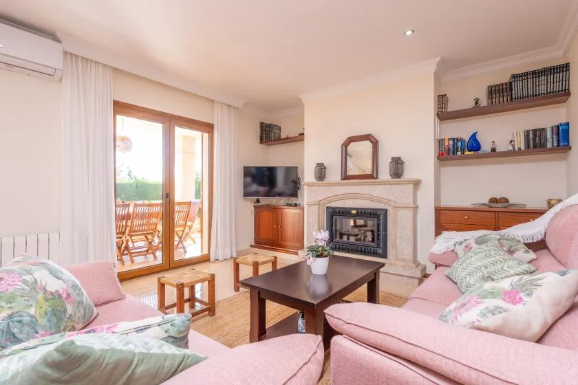 A bright living room with pink seating, a fireplace, and glass doors opening to a balcony.