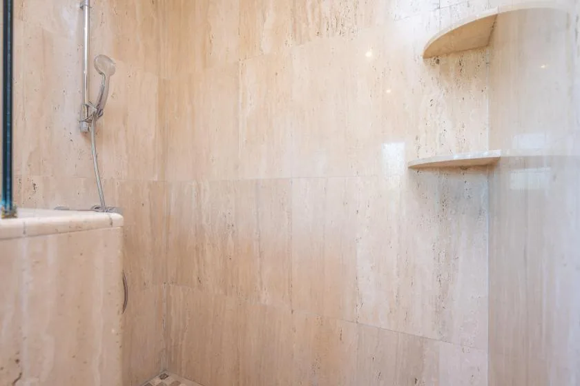 A shower area with pale stone walls and a mounted showerhead.