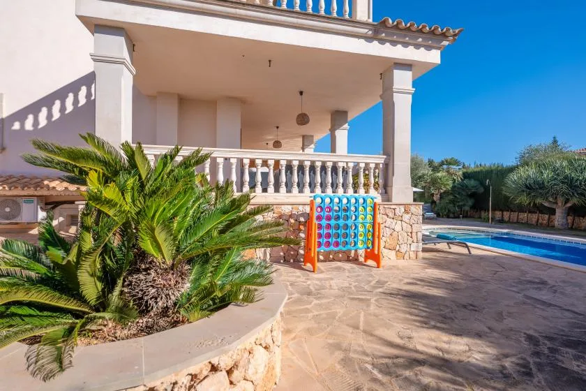 A covered patio overlooks a swimming pool, with a colorful game panel beside the railing.