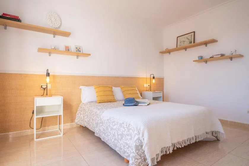 A bedroom with a bed dressed in white linens and wooden wall shelves.