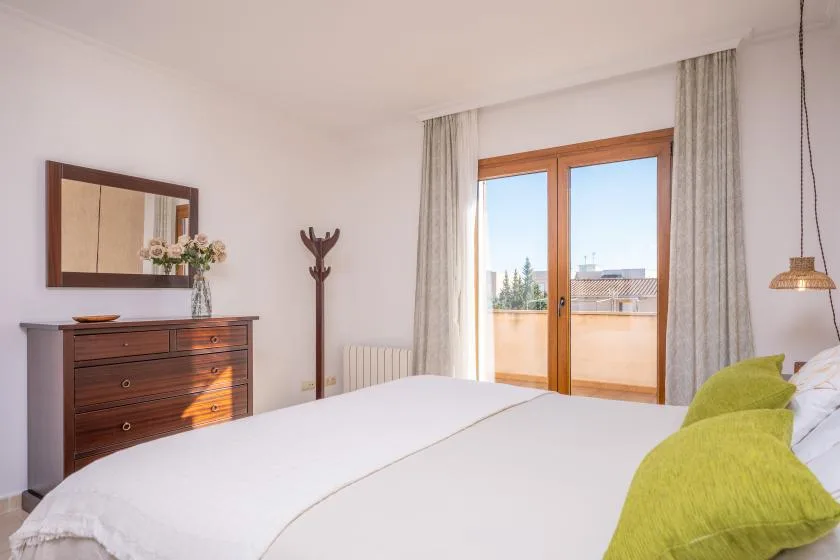 A bedroom with a bed, a dresser, and glass doors opening to a balcony.