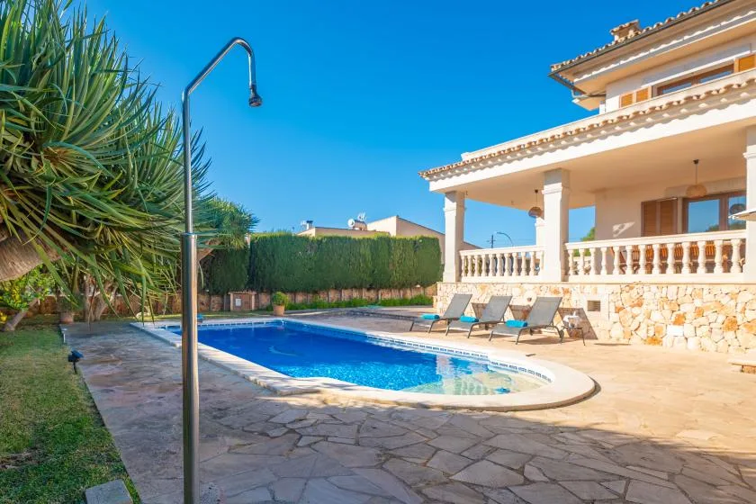 An outdoor swimming pool sits beside a covered patio and several lounge chairs.
