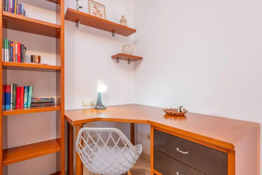 A wooden desk with a white chair sits beside built-in bookshelves.