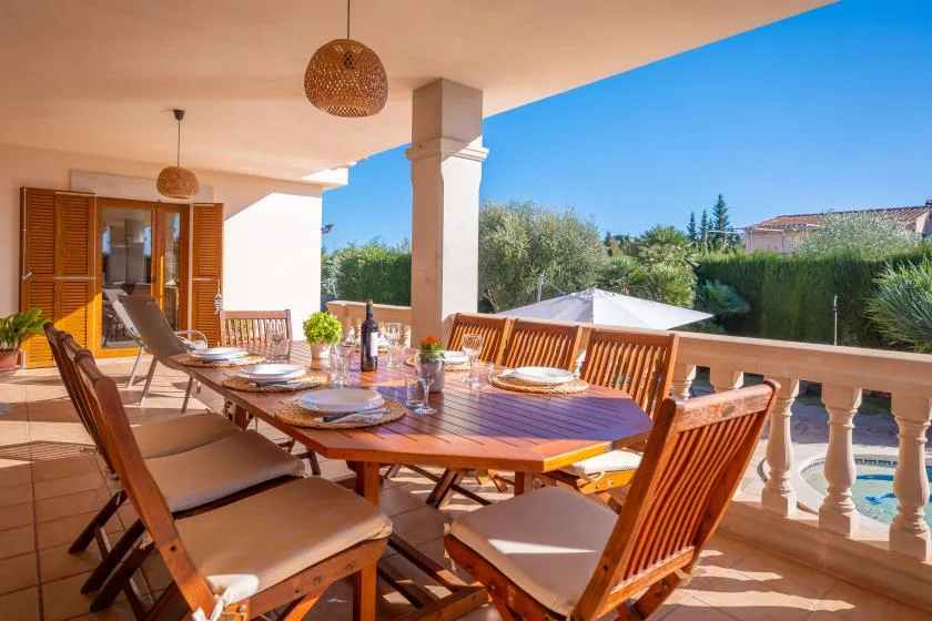 A covered outdoor dining area with a long wooden table and surrounding seating.