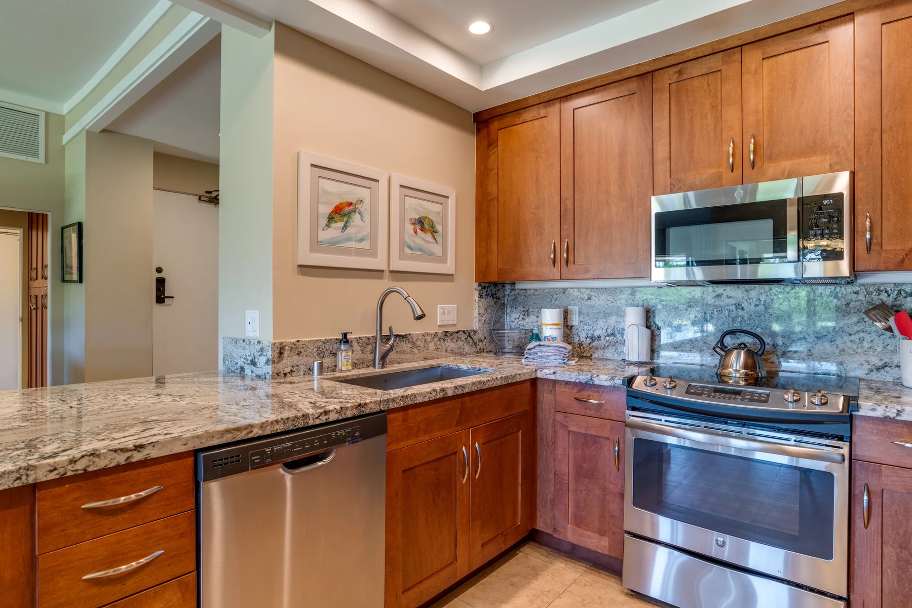 Una cocina con gabinetes de madera, encimeras de piedra y electrodomésticos de acero inoxidable.
