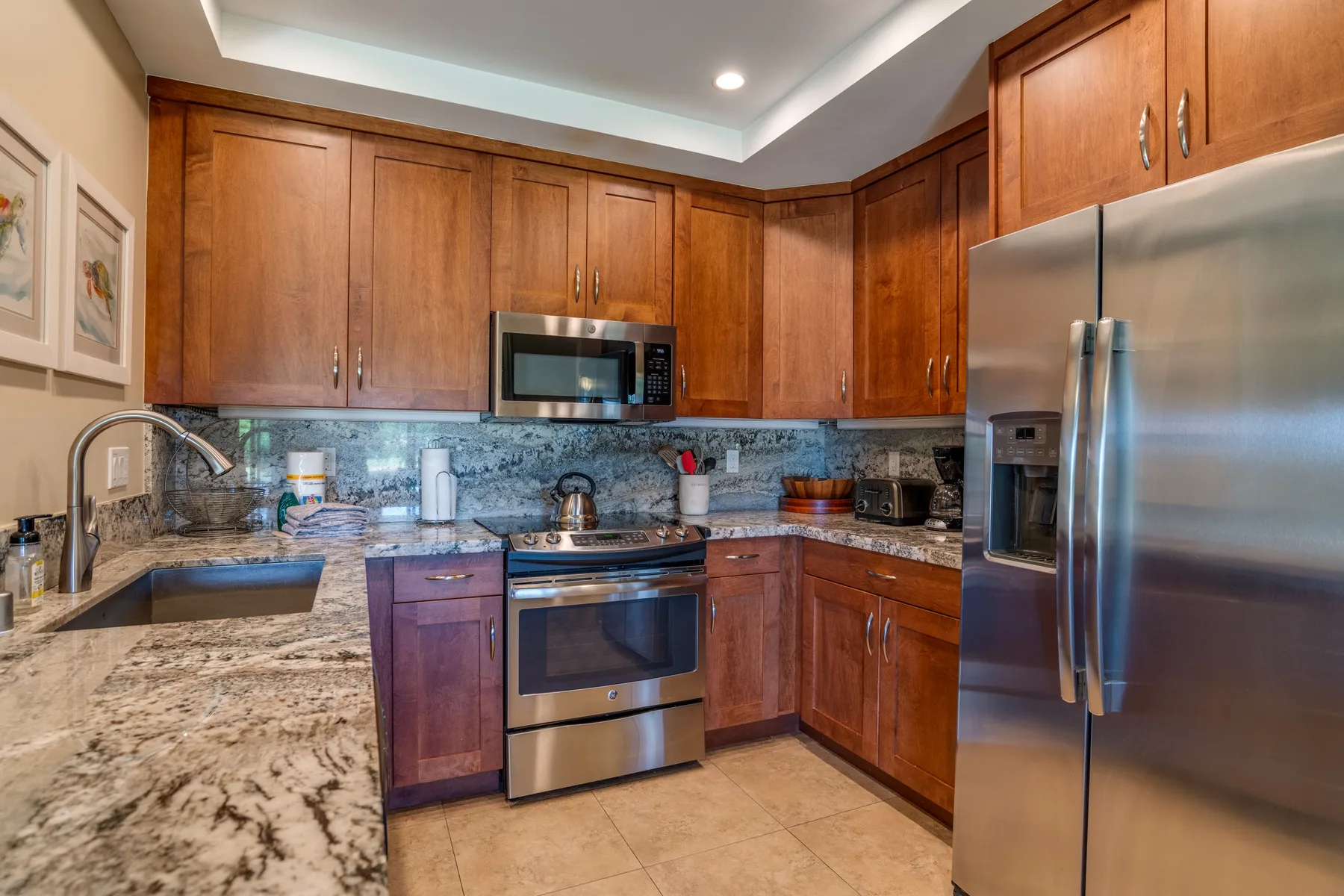 Una cocina con gabinetes de madera, encimeras de piedra y electrodomésticos de acero inoxidable.