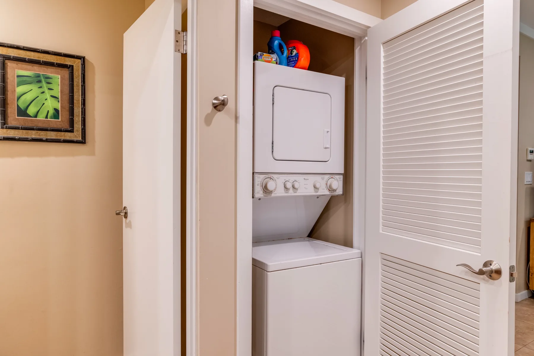 Un armario de lavandería con lavadora y secadora apiladas detrás de puertas abiertas.