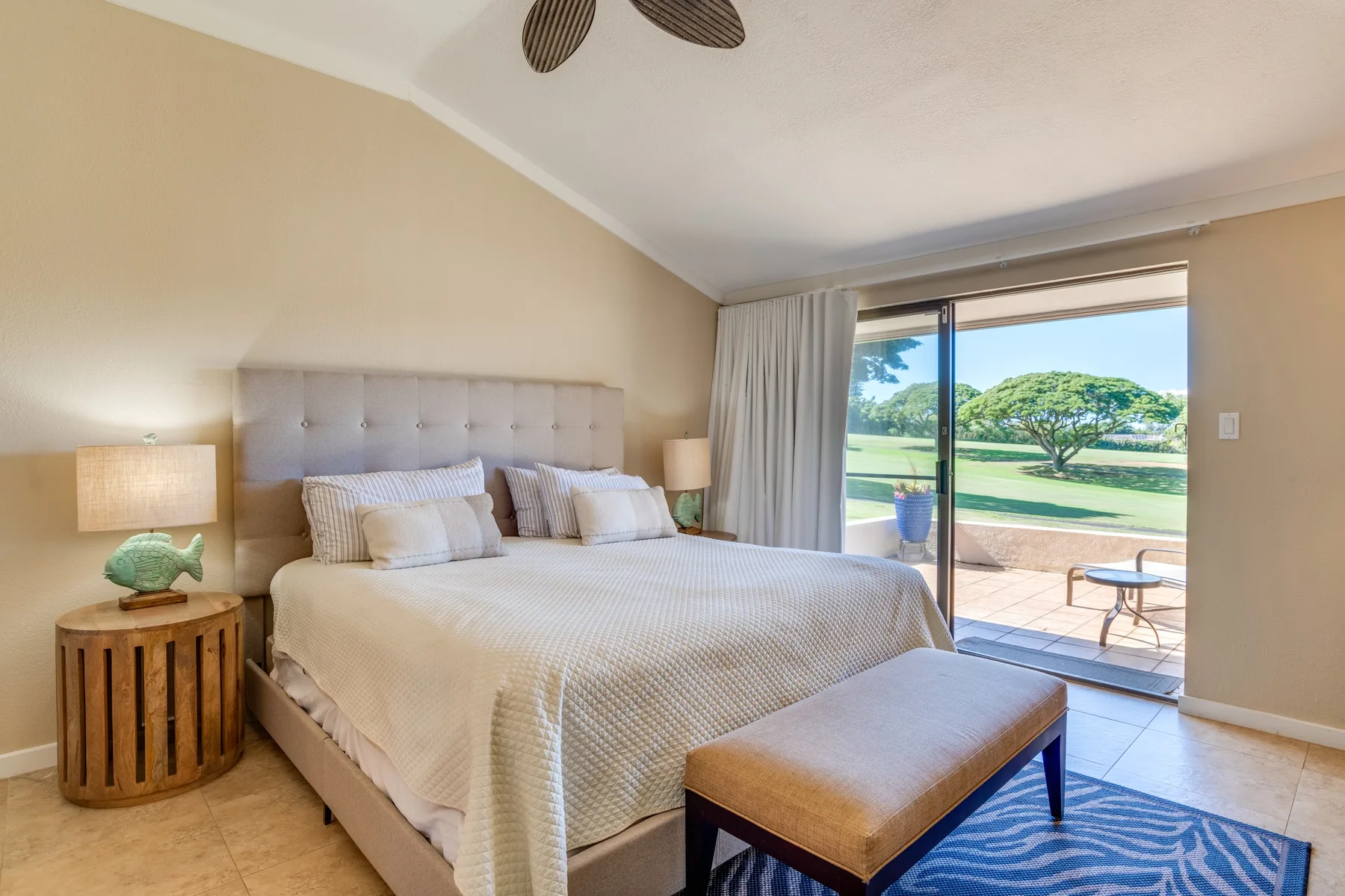 Un dormitorio con una cama bien tendida junto a una puerta de vidrio que da a un patio.