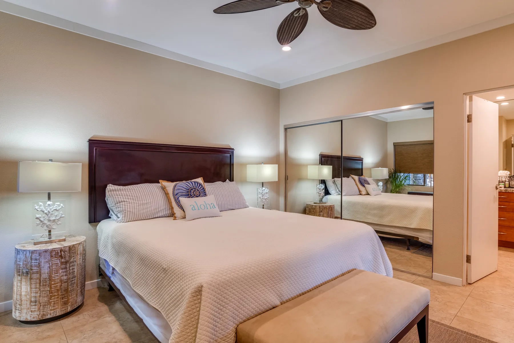 Un dormitorio con una cama grande, puertas de armario con espejo y un banco acolchado.