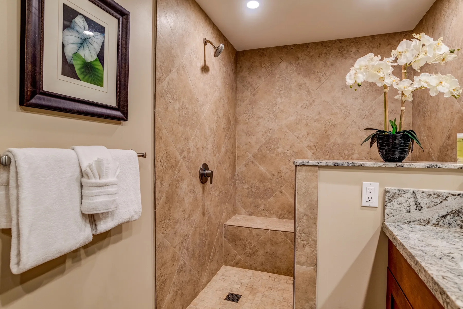 Un baño con una ducha de azulejos y una orquídea blanca sobre la encimera.