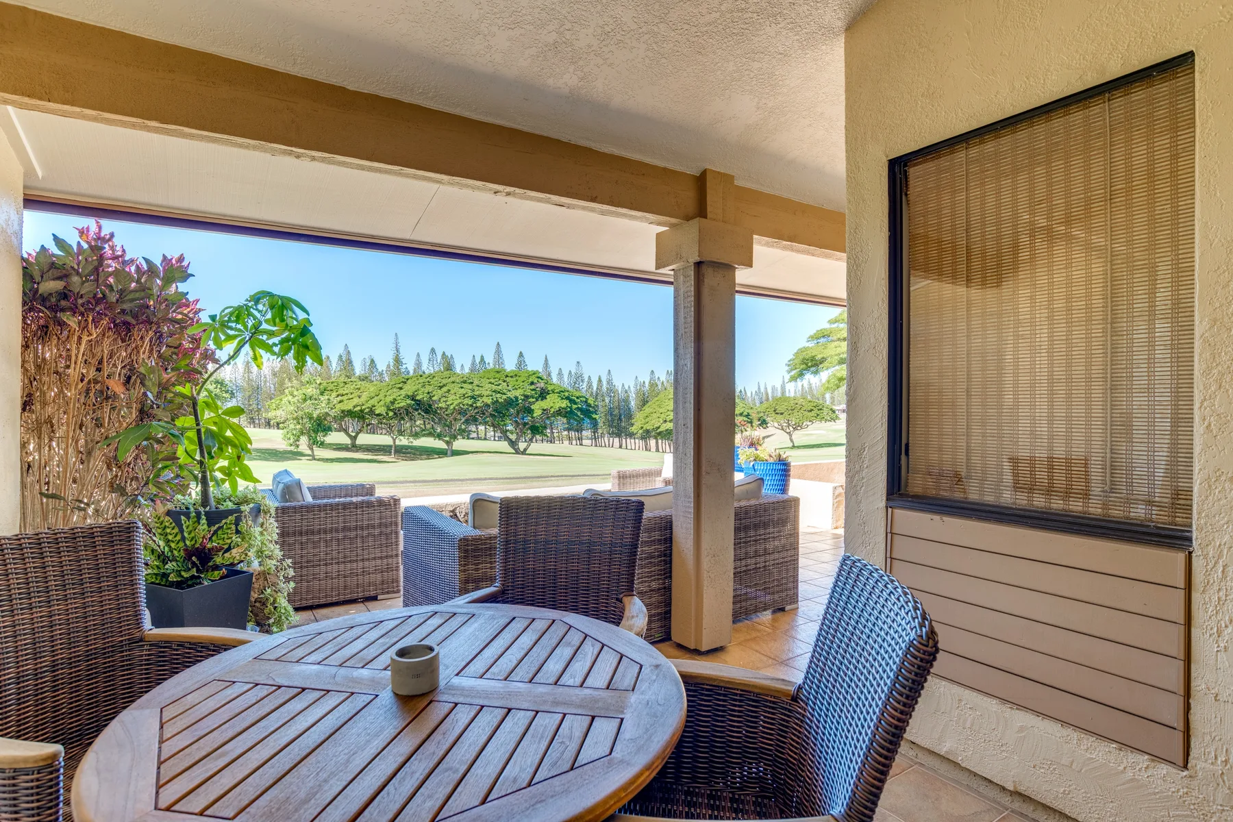 Una zona cubierta de comedor al aire libre con mesa de madera y asientos de mimbre da a un césped.