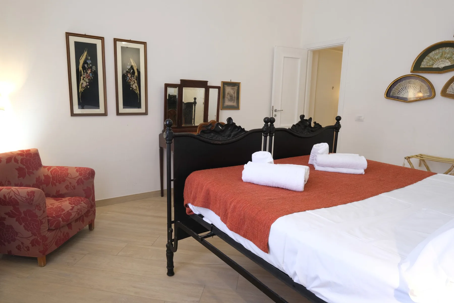 A bedroom with a dark bed, rust-colored coverlet, and folded white towels.