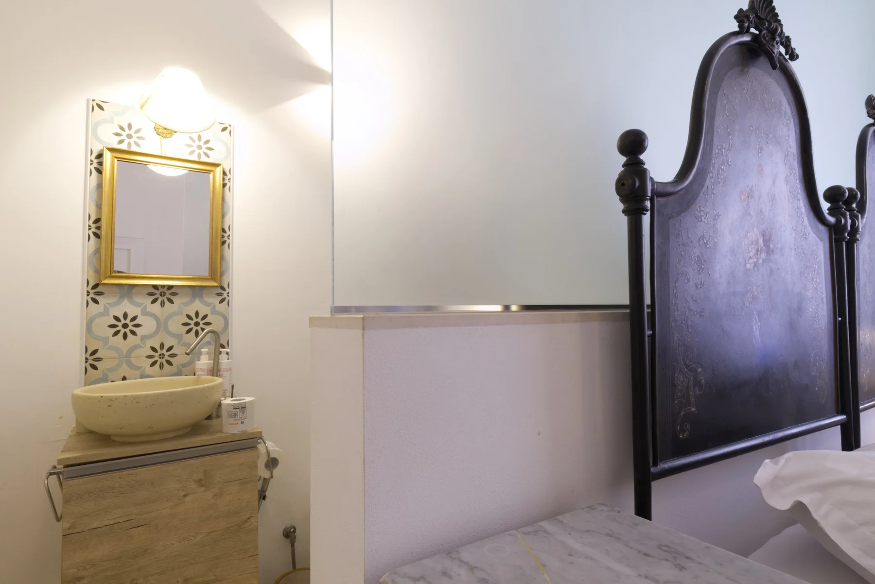 A bedroom with a tall dark headboard and a washbasin area beside the bed.