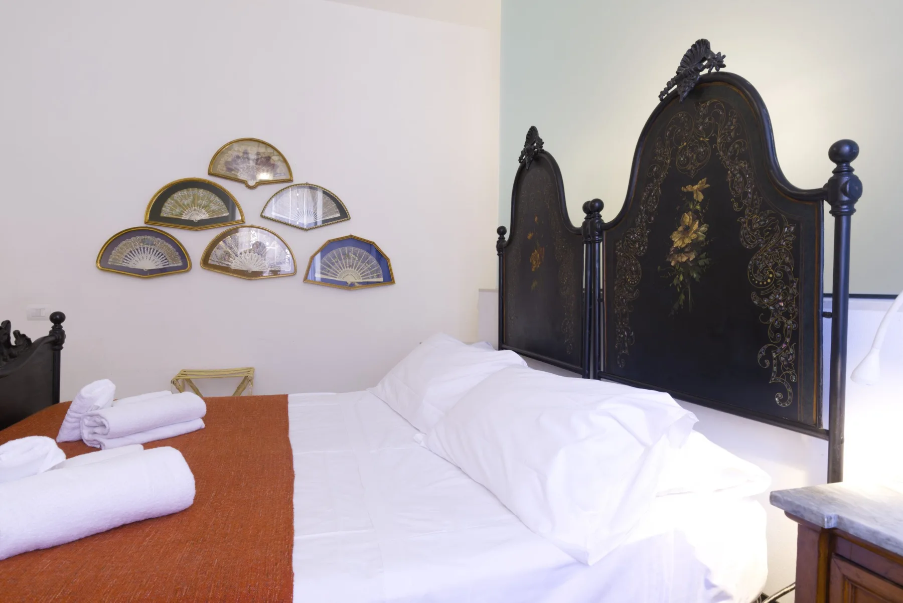 A bedroom with a white bed, dark ornate headboard, and folded towels.