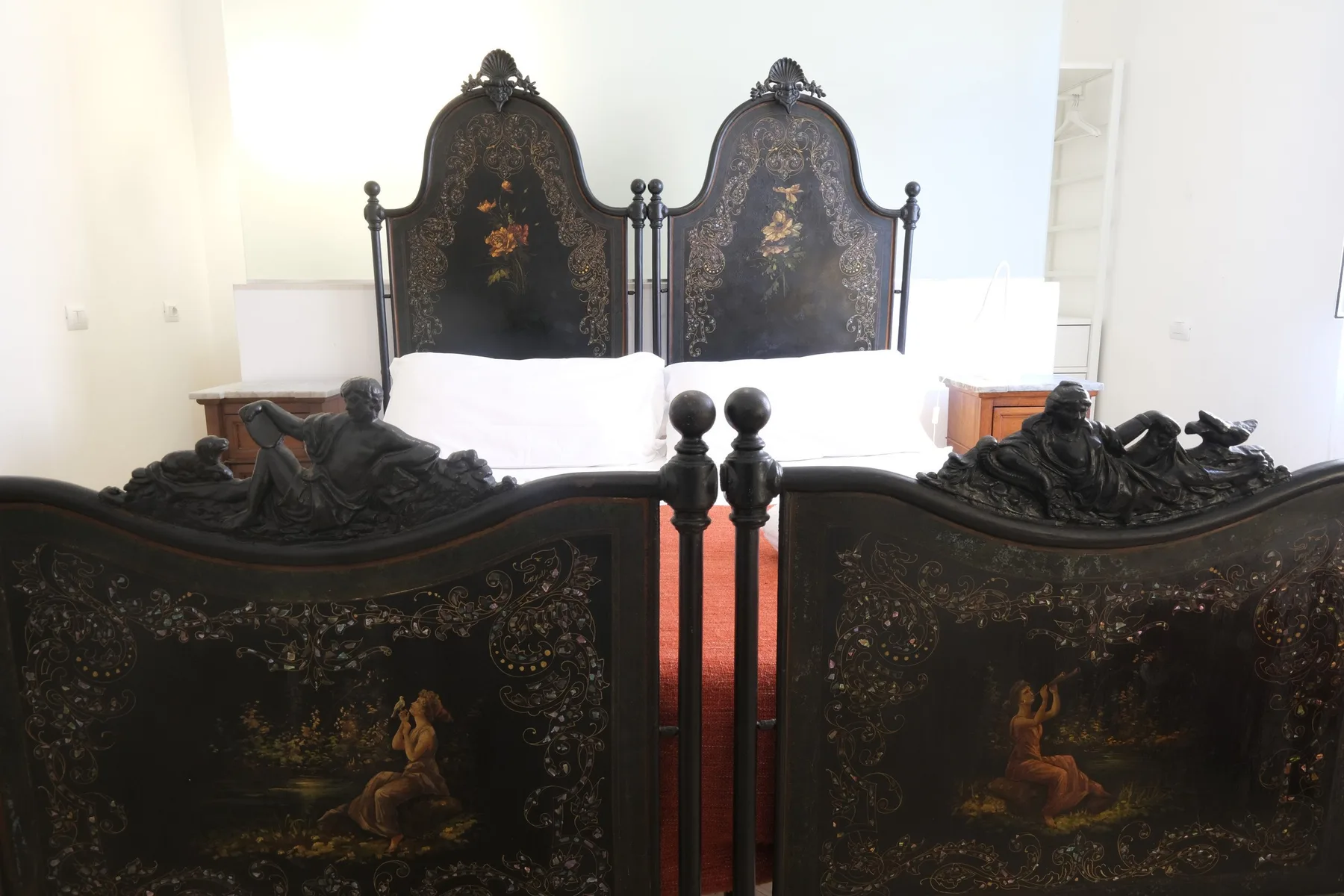 A bedroom with two ornate dark beds and white bedding.