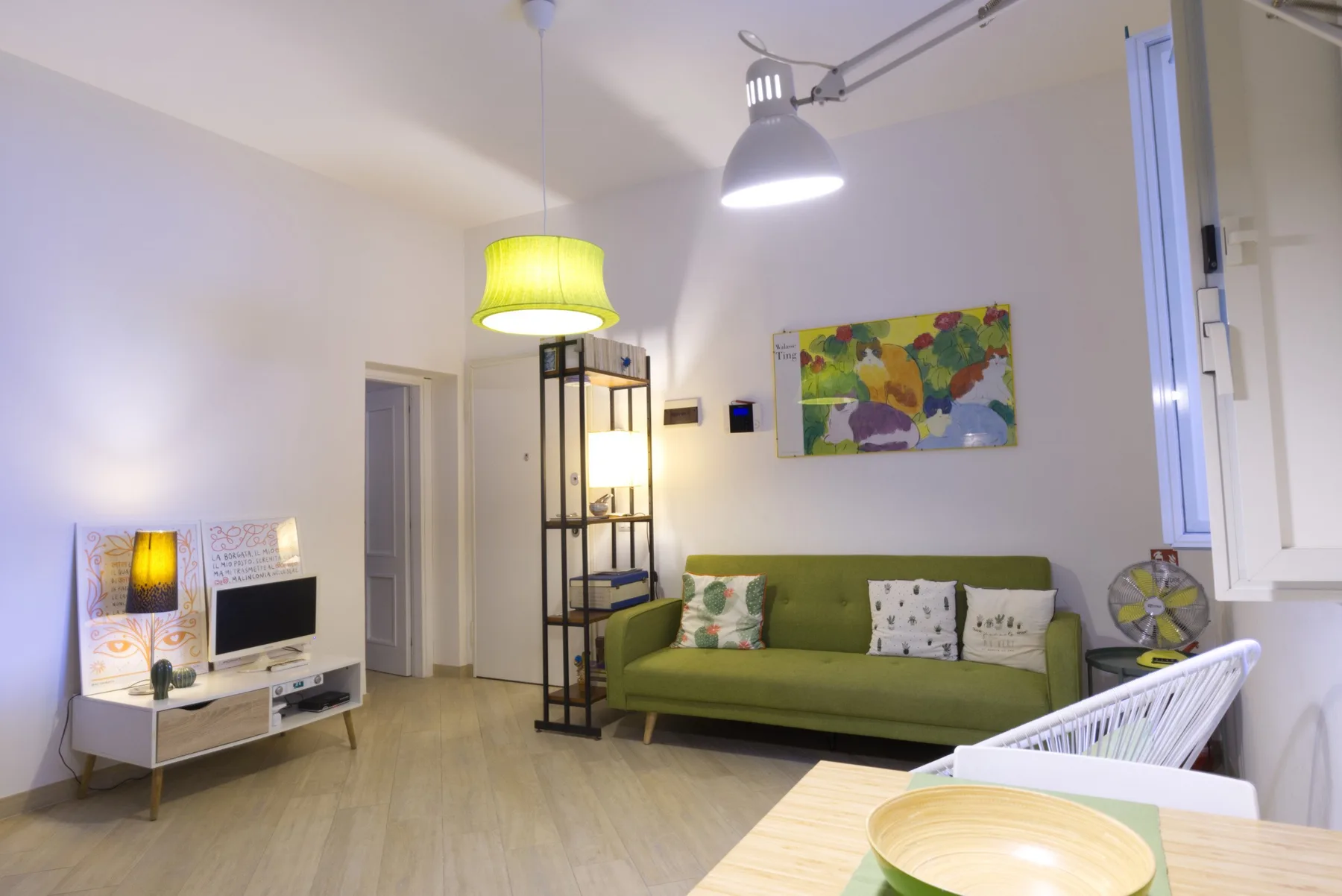 Una sala de estar con asientos verdes, un televisor y arte colorido en la pared.