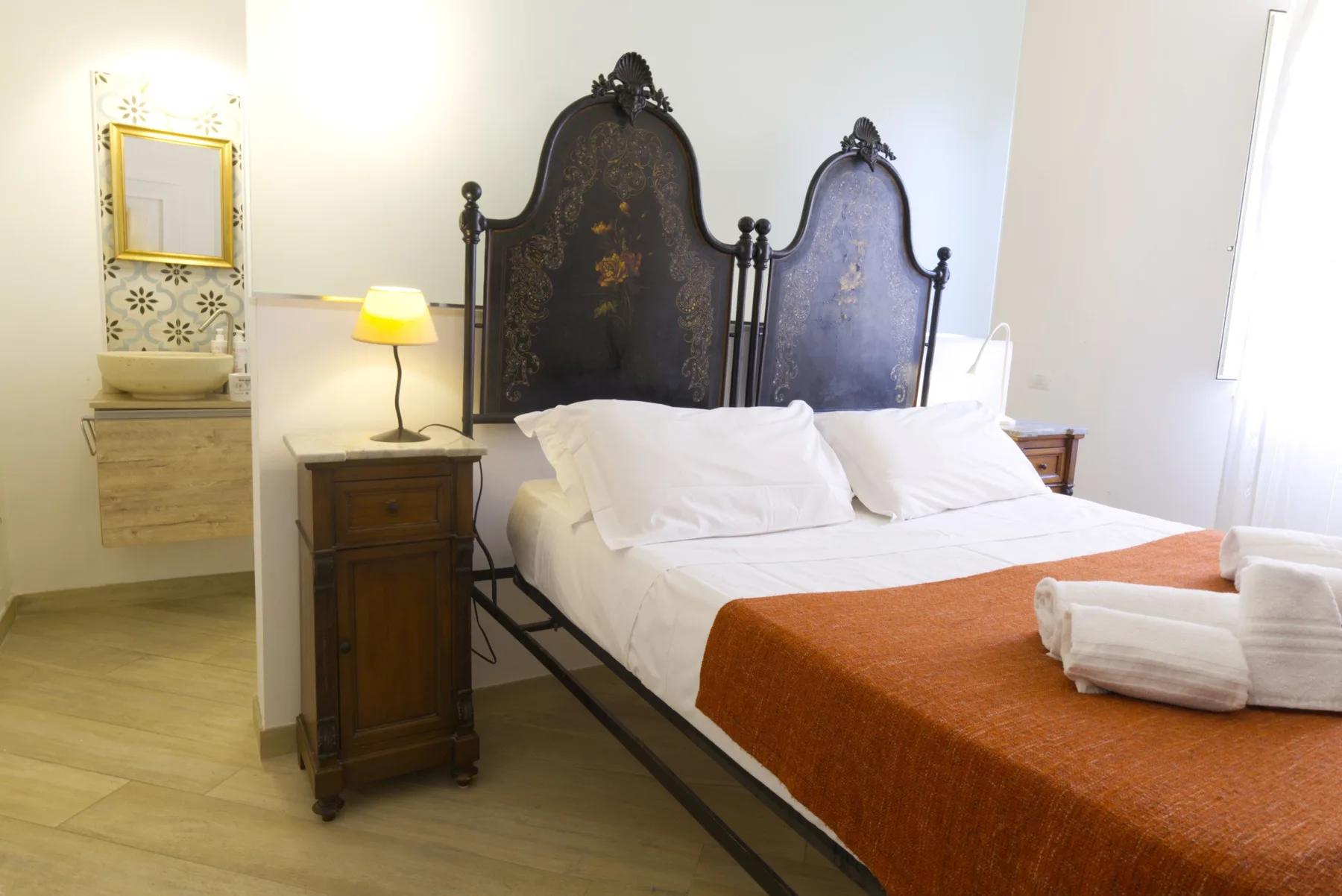A bedroom with a large bed, white bedding, and a rust-colored cover.