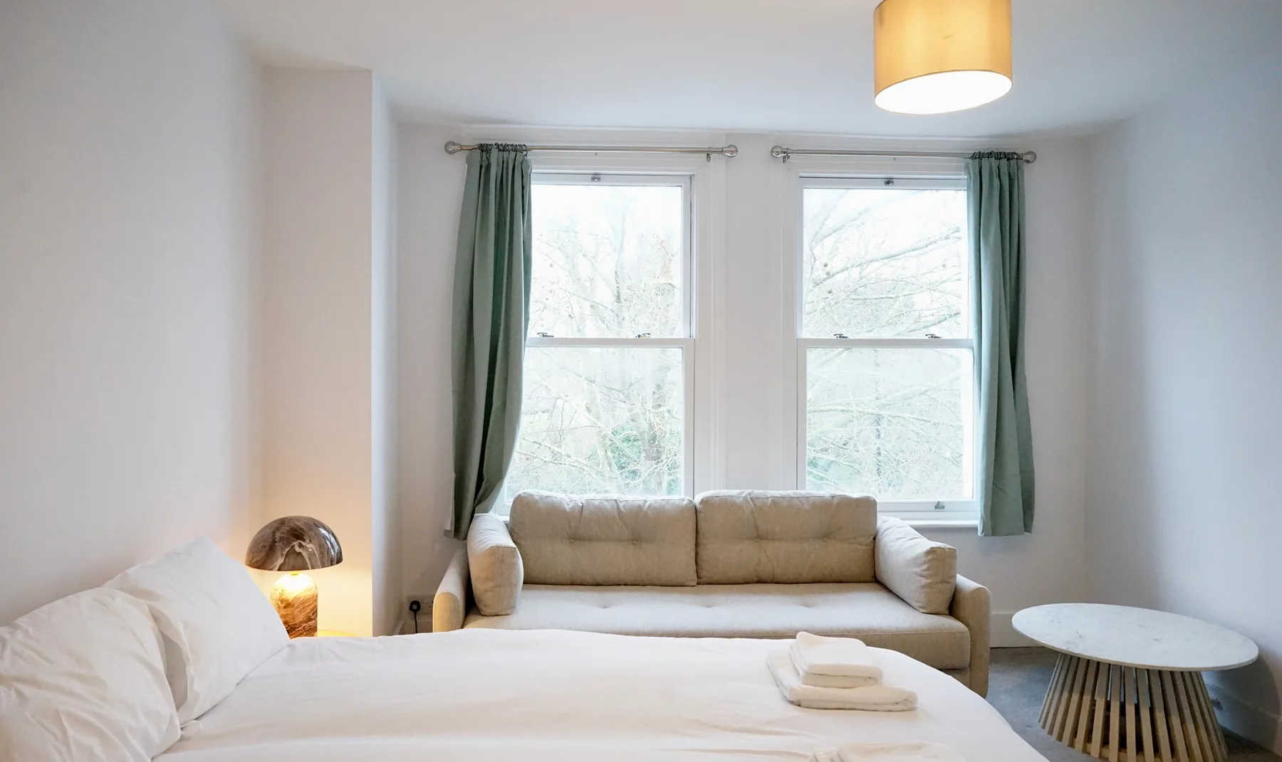 A bright bedroom with a bed and a seating area beside two windows.