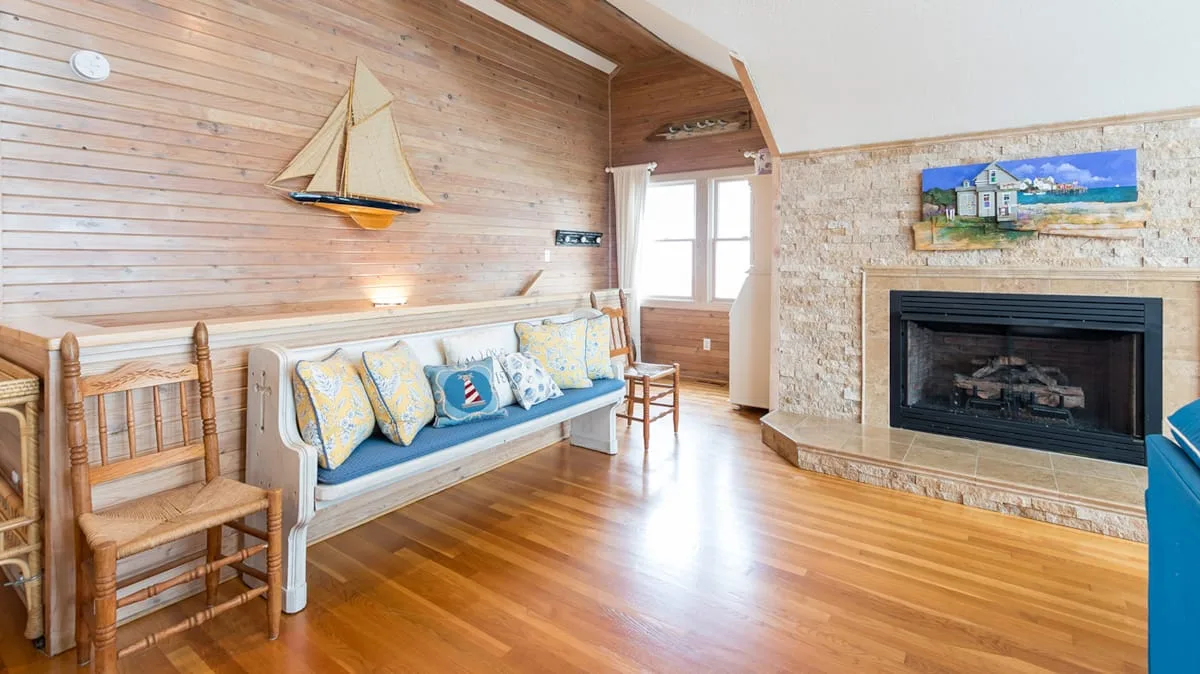 Una sala con paredes de madera tiene un banco acolchado junto a una chimenea de piedra.